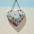 Heart-shaped wooden plaque with floral design hanging on a light blue and beige background