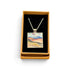 A square pendant necklace displayed in an open tan gift box with a black insert. The pendant features a colorful landscape painting with blue, pink, yellow, and green tones, suspended from a silver-toned chain.