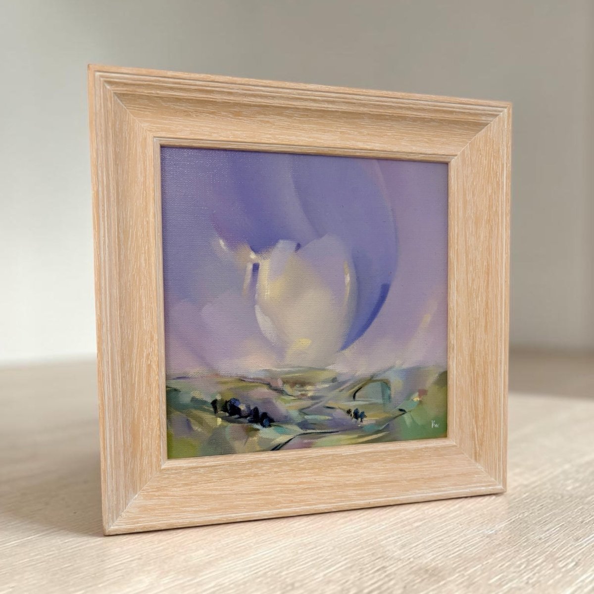 A square framed abstract landscape painting featuring a white bird silhouette against a purple and blue sky with green and yellow ground details, housed in a light natural oak frame.