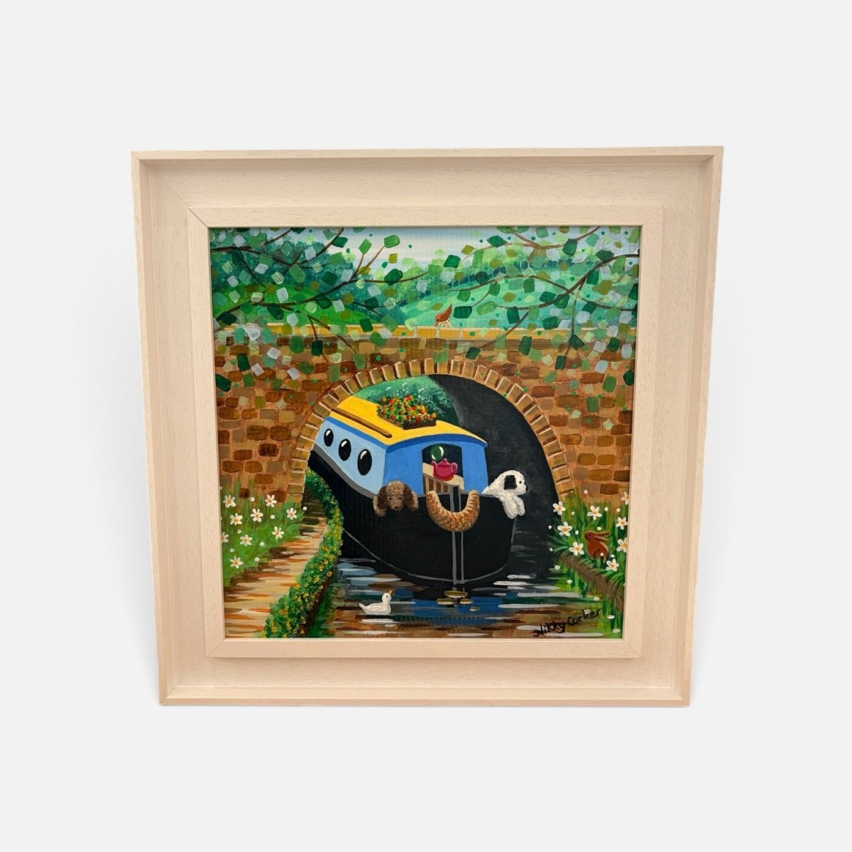 A framed colorful painting of a blue and yellow boat traveling through a tunnel under a bridge, surrounded by green foliage and a brick archway, shown in a light wood frame against a white background.