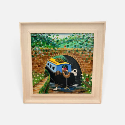 A framed colorful painting of a blue and yellow boat traveling through a tunnel under a bridge, surrounded by green foliage and a brick archway, shown in a light wood frame against a white background.