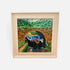 A framed colorful painting of a blue and yellow boat traveling through a tunnel under a bridge, surrounded by green foliage and a brick archway, shown in a light wood frame against a white background.