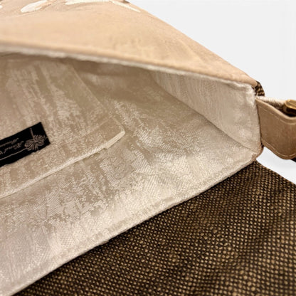 Close-up of a beige fabric handbag showing the interior lining and a black brand label, with a brown woven exterior visible at the bottom.