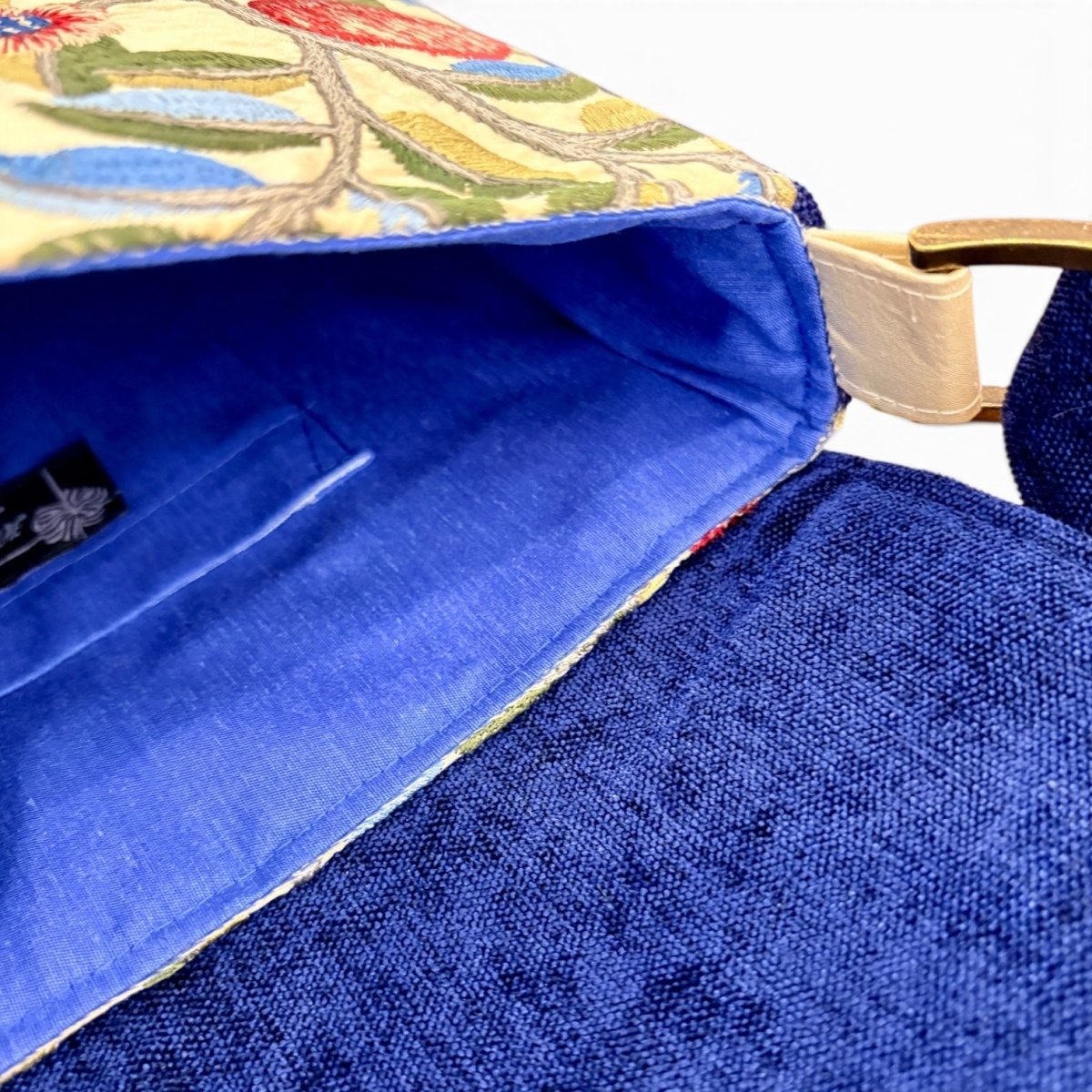 Close-up of a blue fabric handbag showing the interior lining, floral embroidered exterior, and a light beige strap attachment.