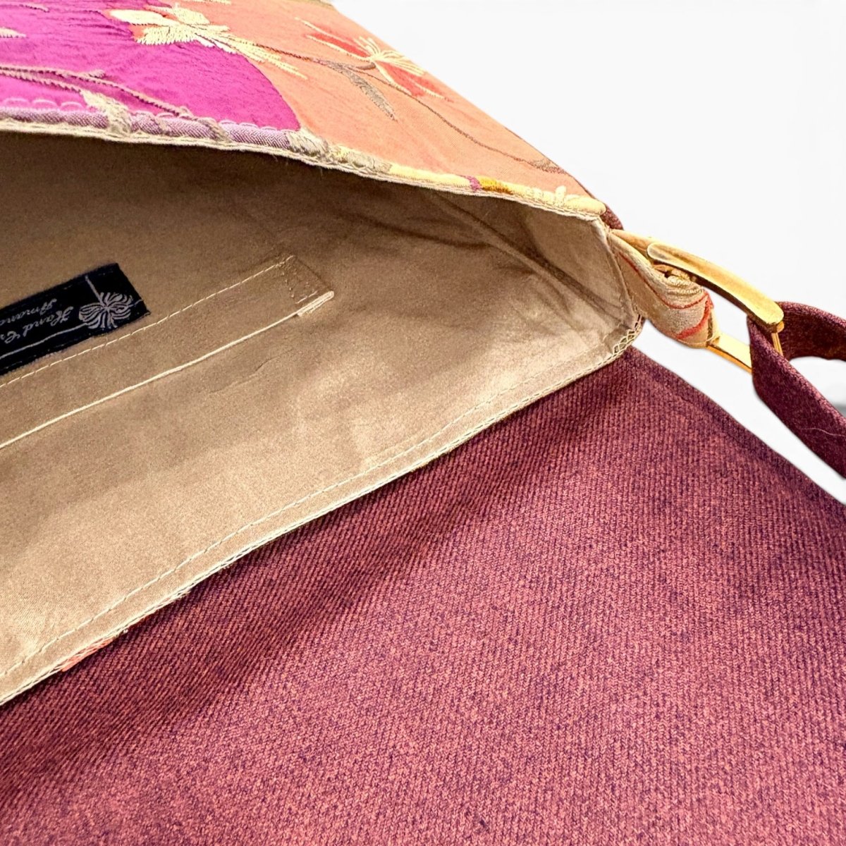 Close-up of a fabric shoulder bag showing a pink and orange floral patterned exterior, a tan interior lining, and a dark burgundy strap with a gold metal ring.
