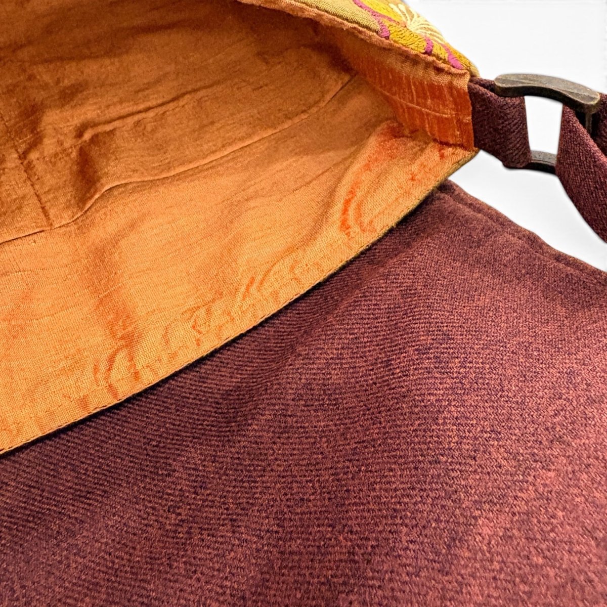 Close-up of a fabric bag or pouch showing a rust-orange satin-like interior lining and a textured burgundy exterior, with a dark metal clasp visible at the top right.
