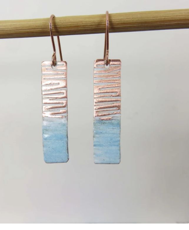 Pair of earrings with textured copper top and blue bottom on a stick against a light background