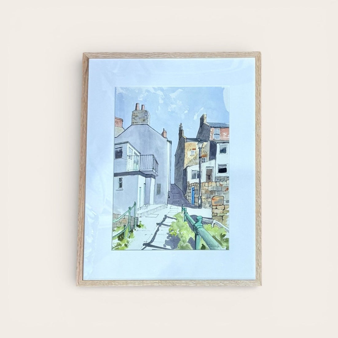 Framed artwork of a coastal scene with houses and a blue sky.