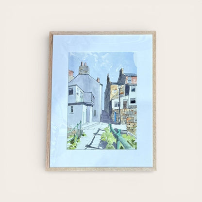 Framed artwork of a coastal scene with houses and a blue sky.