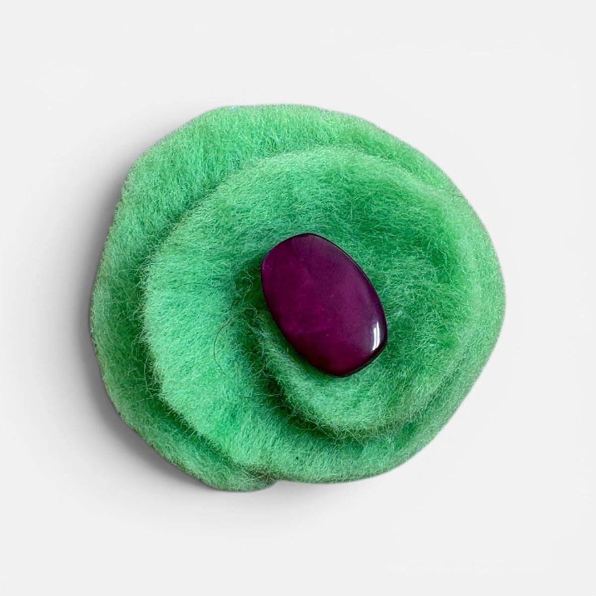 Green felt brooch with a purple stone on a light gray background