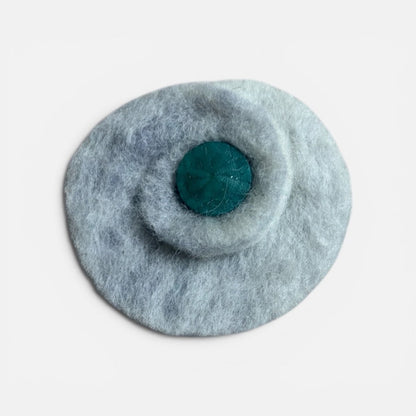 Round gray felted product with a central teal circle on a light gray background