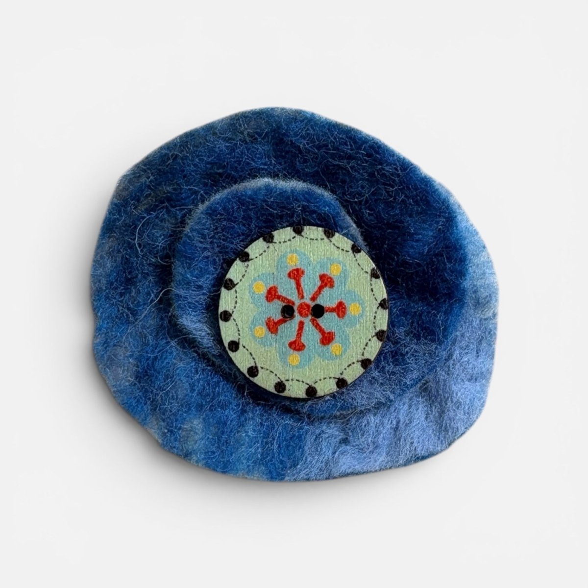 Blue felted flower with a circular embroidered center on a white background