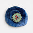 Blue felted flower with a circular embroidered center on a white background