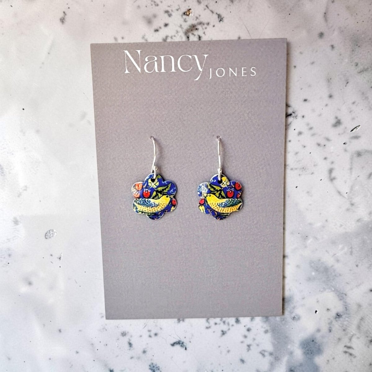 Colorful heart-shaped earrings on a Nancy Jones card against a marble background