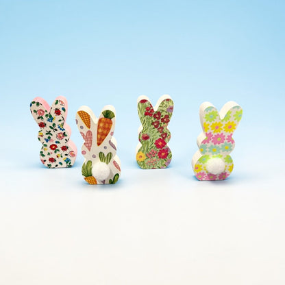 Four colorful wooden bunny figurines with floral and carrot patterns on a light blue background.