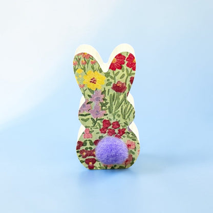 Floral-patterned bunny-shaped toy with a purple pom-pom on a light blue background