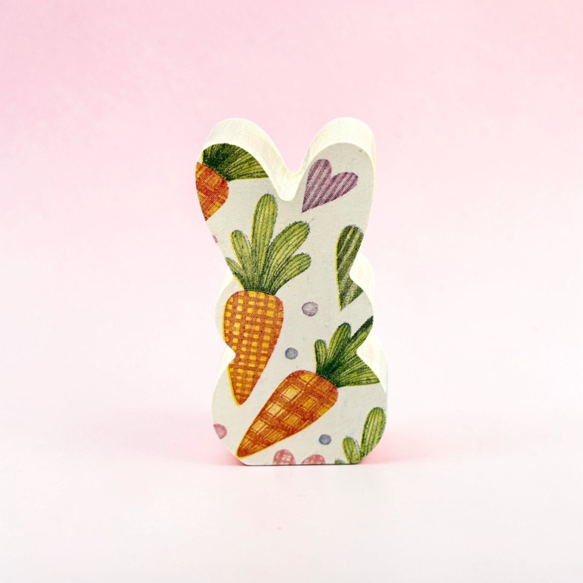 Decorative bunny-shaped item with carrot and leaf design on a pink background