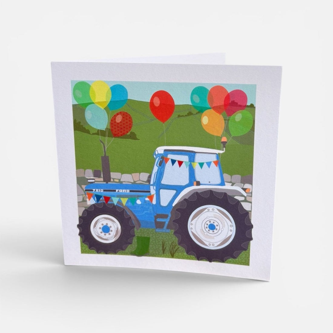 Card with a blue tractor and colorful balloons on a white background