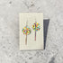 Colorful geometric earrings on a Nancy James card against a textured gray background