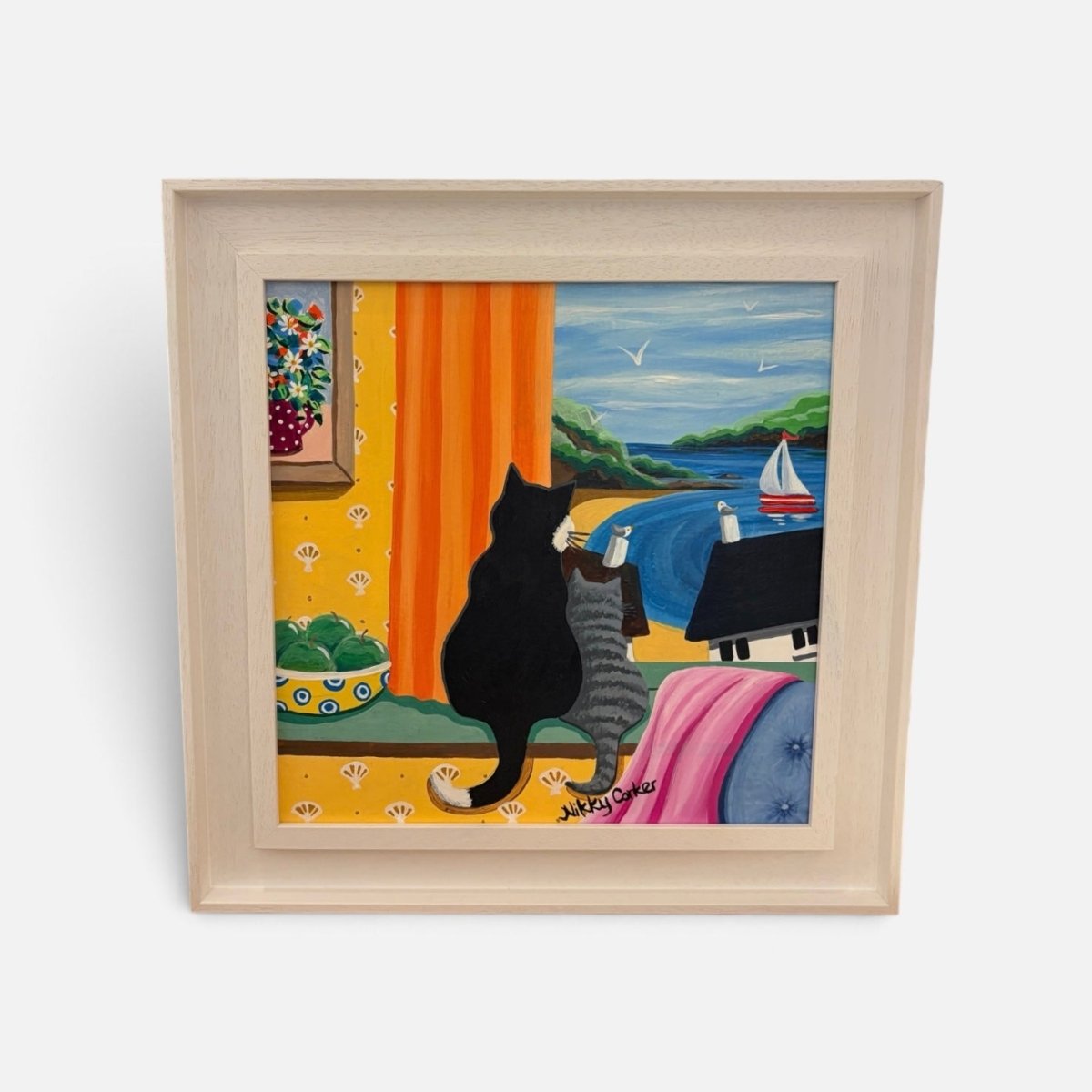 A square framed art print featuring a whimsical painting of two cats sitting by a window looking out at a blue sea and sky, with a sailboat, green hills, and a yellow interior with orange curtains and patterned wallpaper. The artwork is housed in a light natural wood frame and photographed against a clean white background.