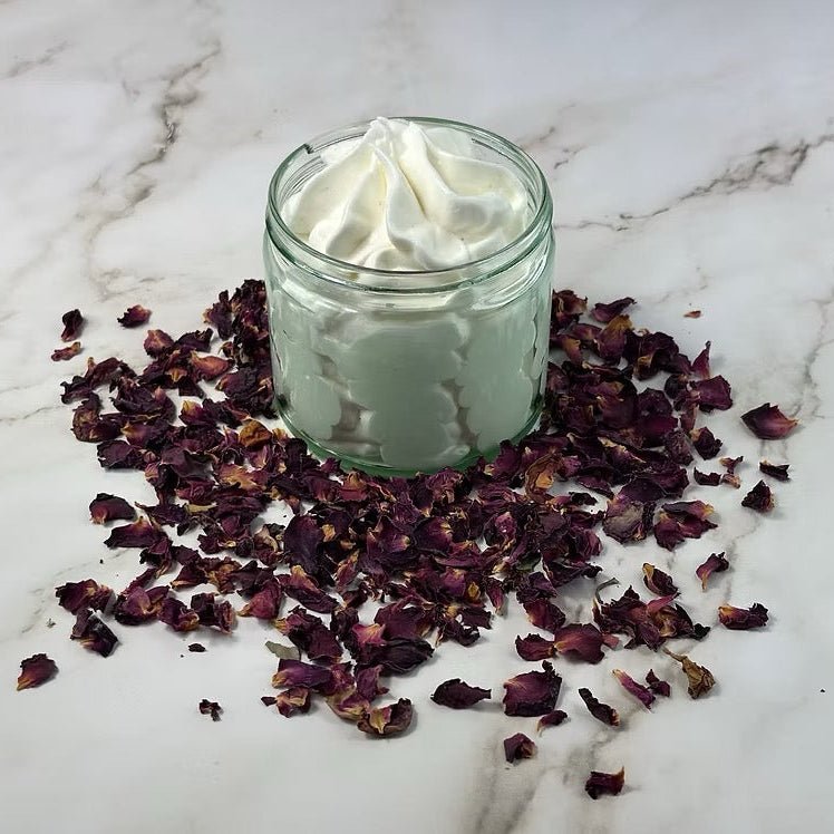 Glass jar of cream surrounded by dried rose petals on a marble surface