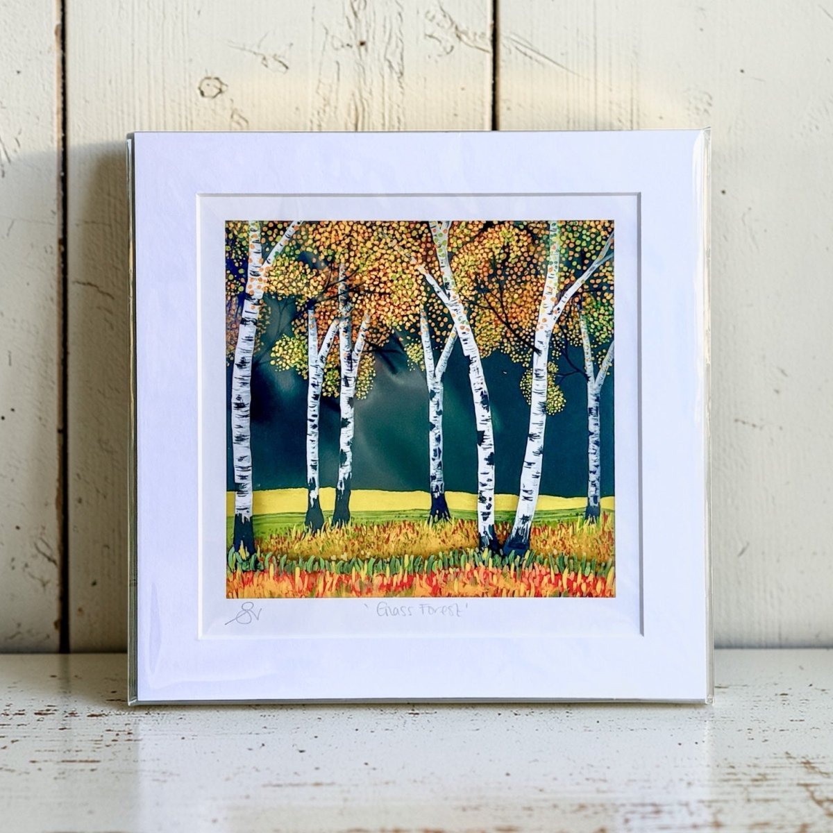 Framed artwork of birch trees with autumn foliage on a wooden surface.