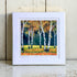 Framed artwork of birch trees with autumn foliage on a wooden surface.