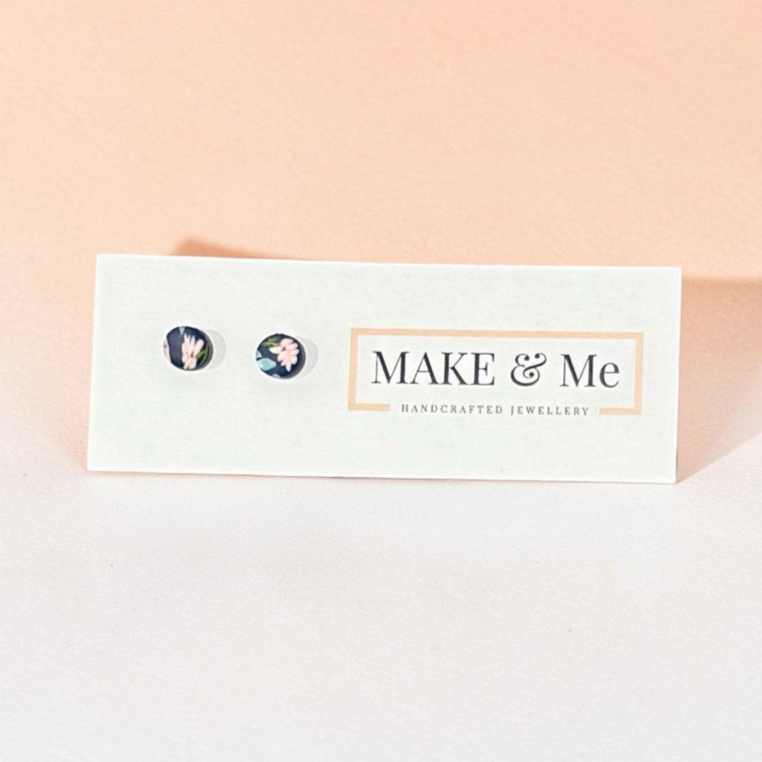 Make &amp; Me earrings on a branded card with a pink background