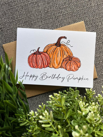 A white greeting card with an illustration of three orange pumpkins and the handwritten text &