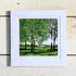 Framed artwork of a green landscape with trees on a wooden surface