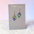 Colorful diamond-shaped earrings on a Nancy Jones card against a light background