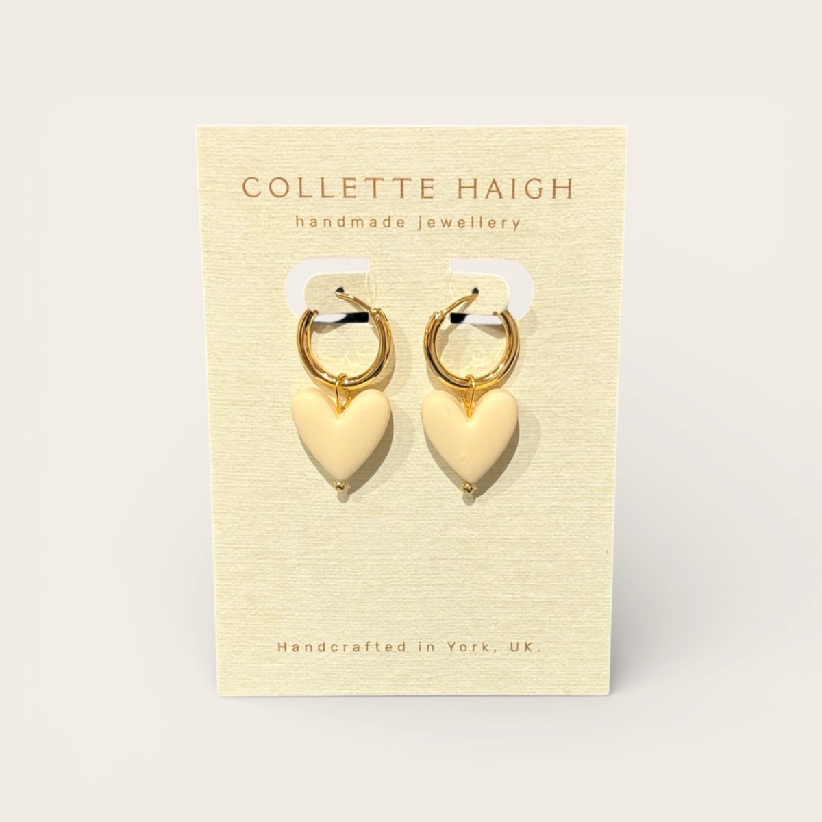 Heart-shaped earrings on a Collette Haigh branded card with a beige background