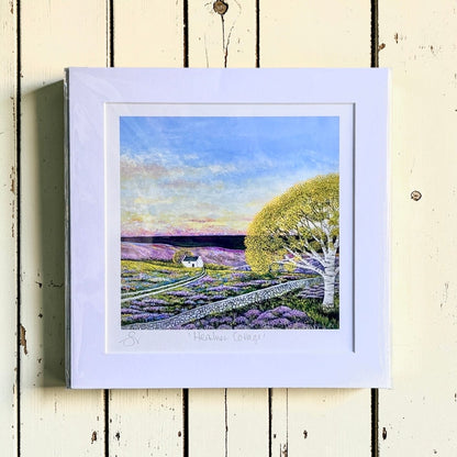 Framed artwork of a landscape with a house, tree, and lavender field on a wooden surface.