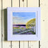 Framed artwork of a landscape with a house, tree, and lavender field on a wooden surface.
