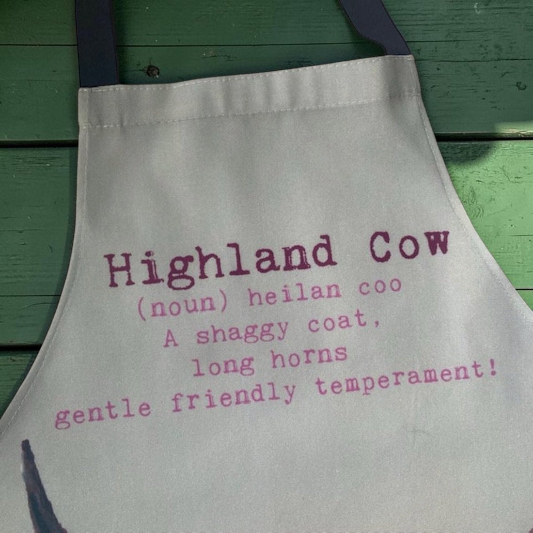 Apron with text about Highland cows on a green wooden background