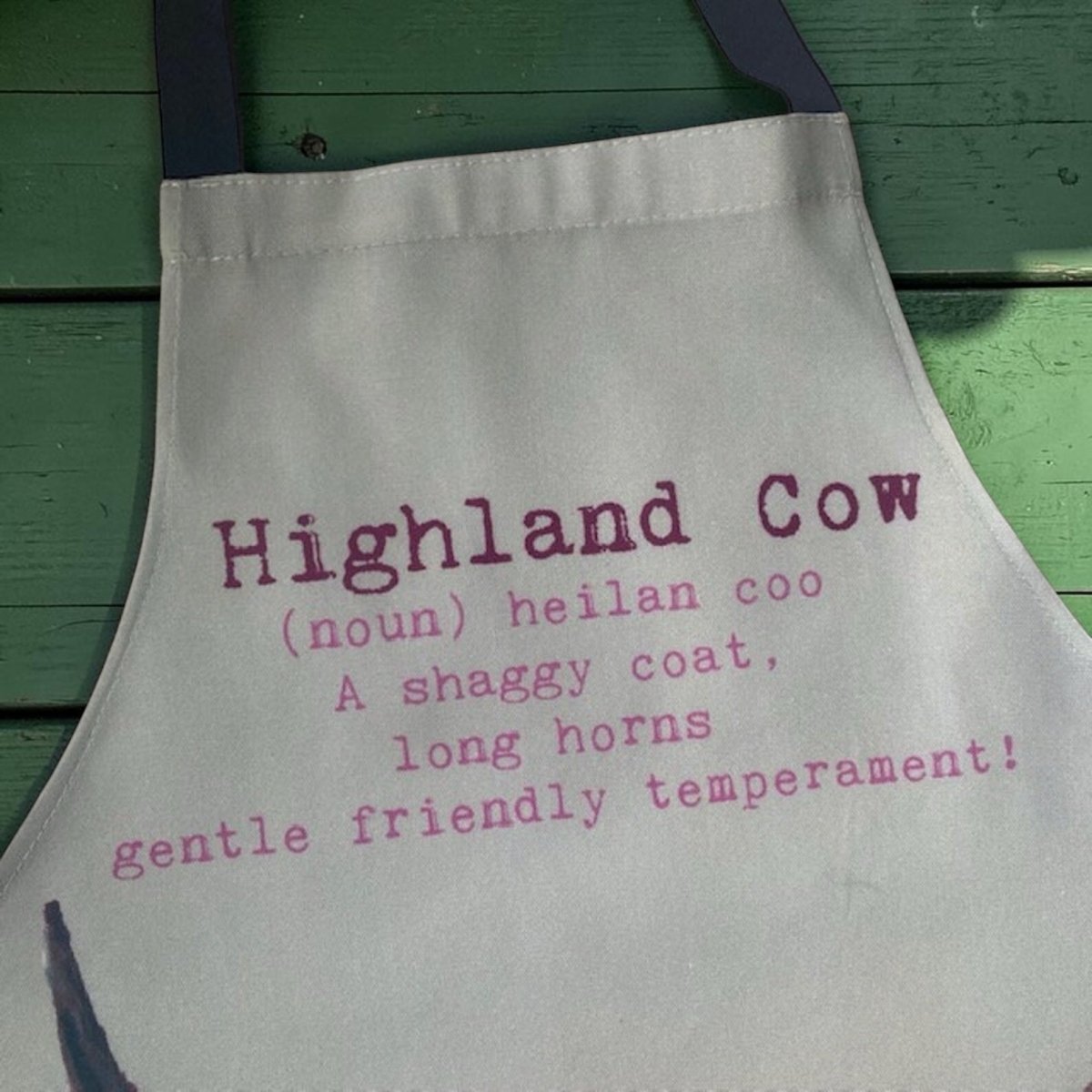 Apron with text about Highland cows on a green wooden background