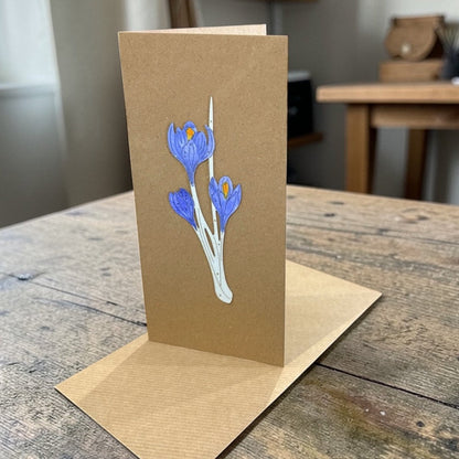 Brown greeting card with blue floral design on a wooden surface