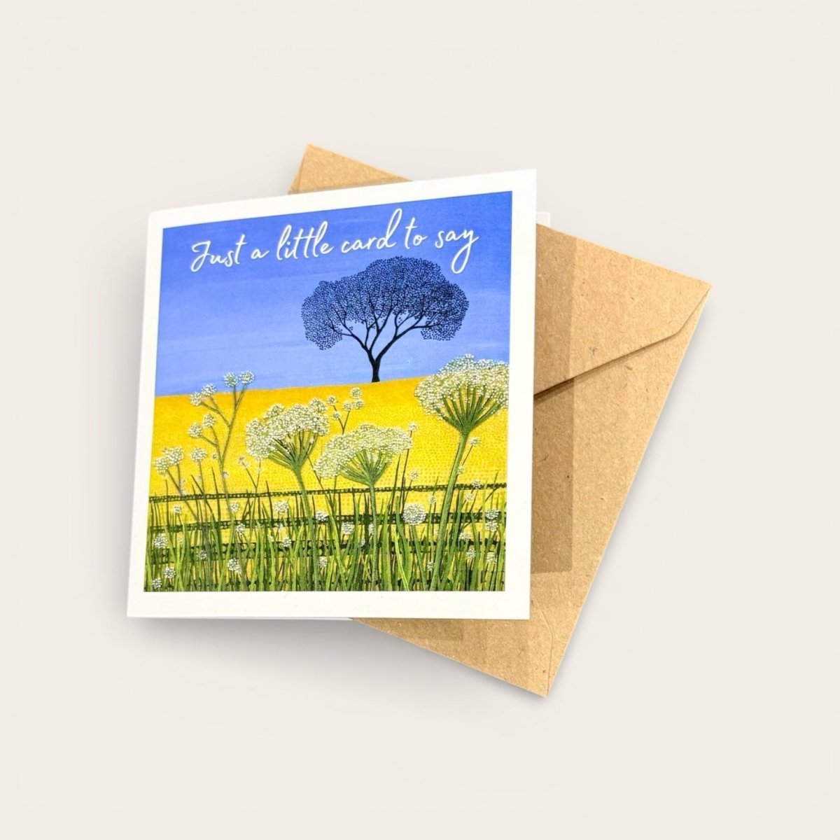Greeting card with a tree and flowers design on a blue background, accompanied by a brown envelope.