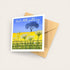 Greeting card with a tree and flowers design on a blue background, accompanied by a brown envelope.