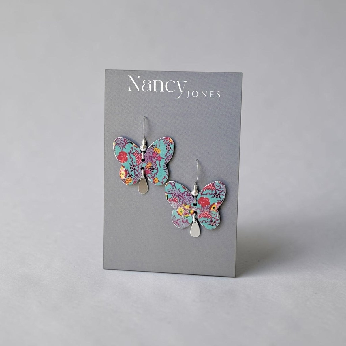 Butterfly earrings on a Nancy Jones branded card against a gray background