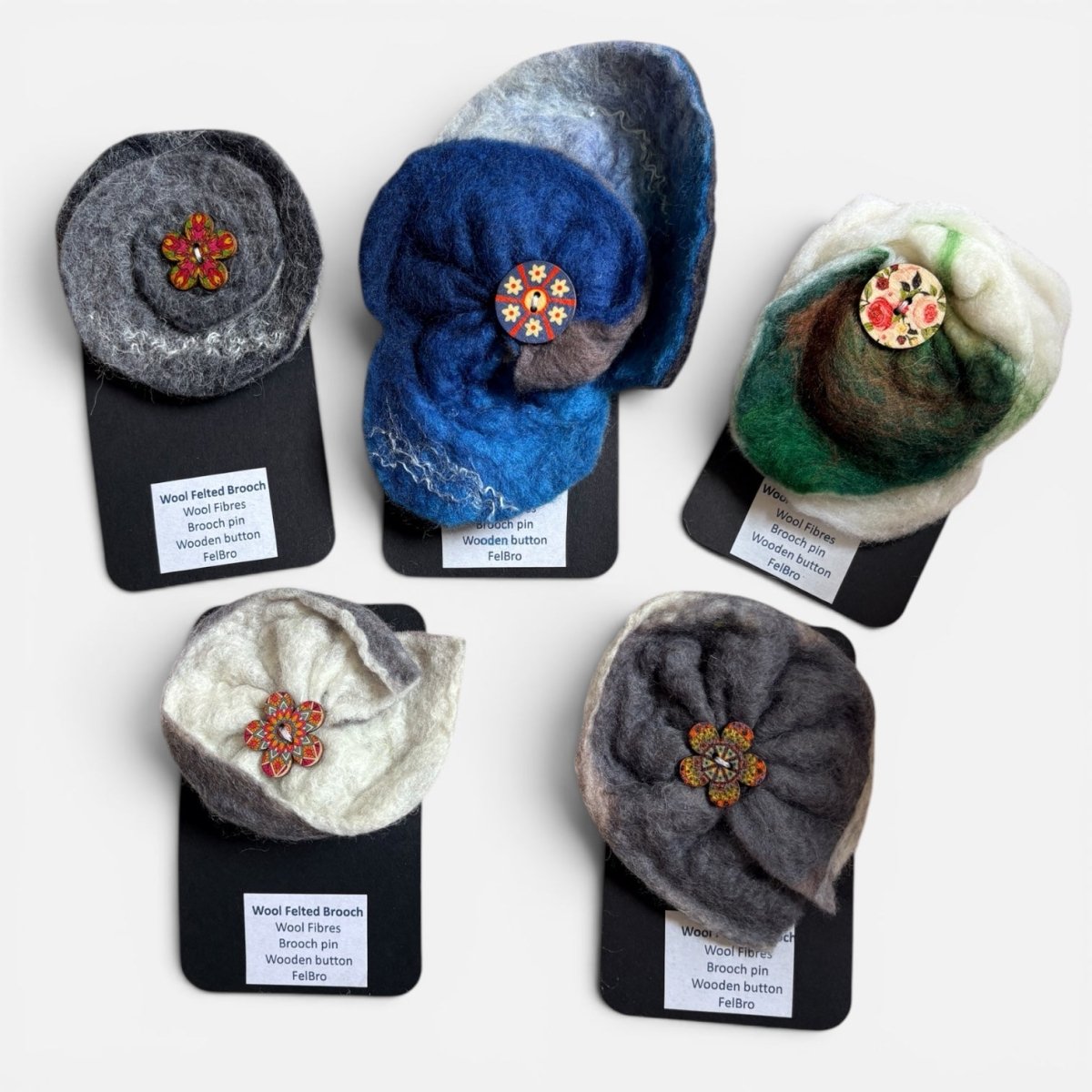 Set of six felted brooches in various colors on display cards with labels.