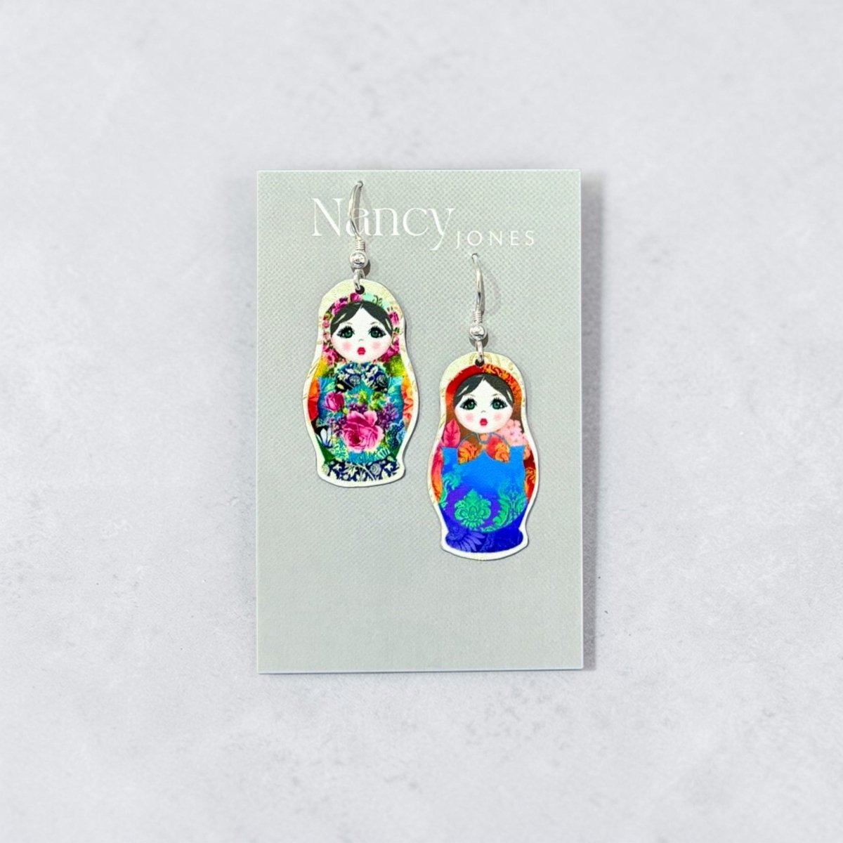 Colorful matryoshka doll earrings on a Nancy Jones card against a light gray background