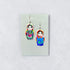 Colorful matryoshka doll earrings on a Nancy Jones card against a light gray background
