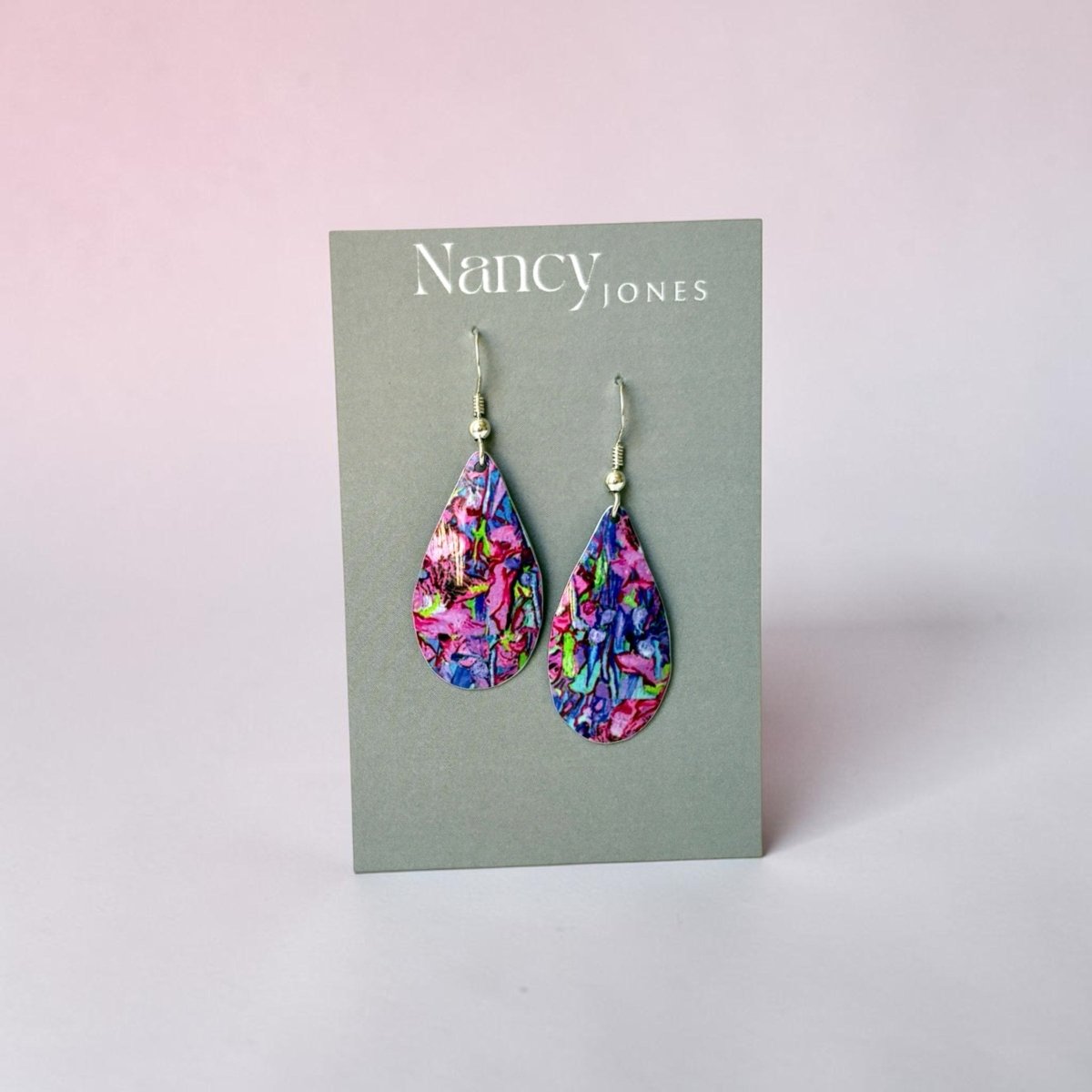 Colorful teardrop earrings on a Nancy Jones card against a light pink background