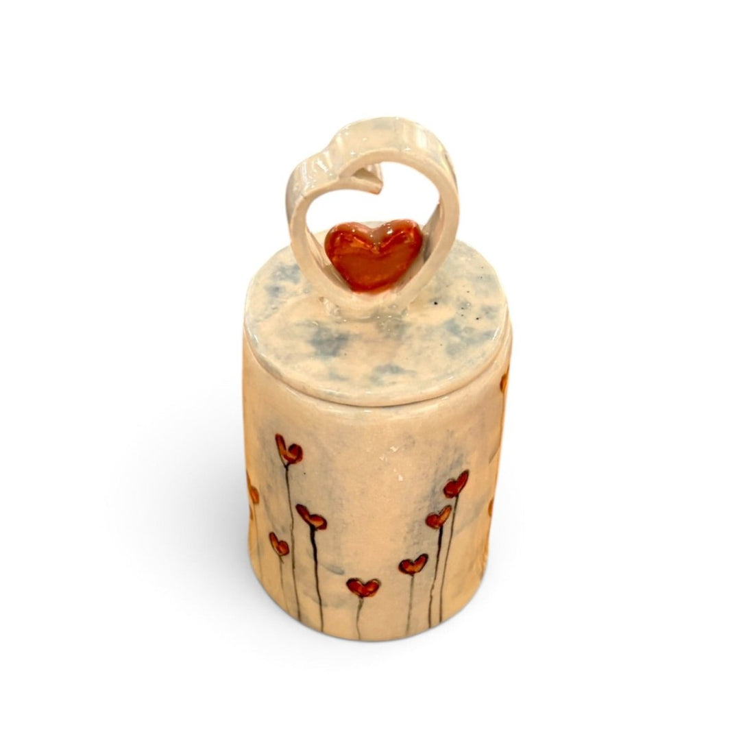A small cylindrical ceramic keepsake box with a lid, decorated with red heart-shaped flowers on a beige background, featuring a heart-shaped ring topper with a red heart in the center, set against a plain white background.