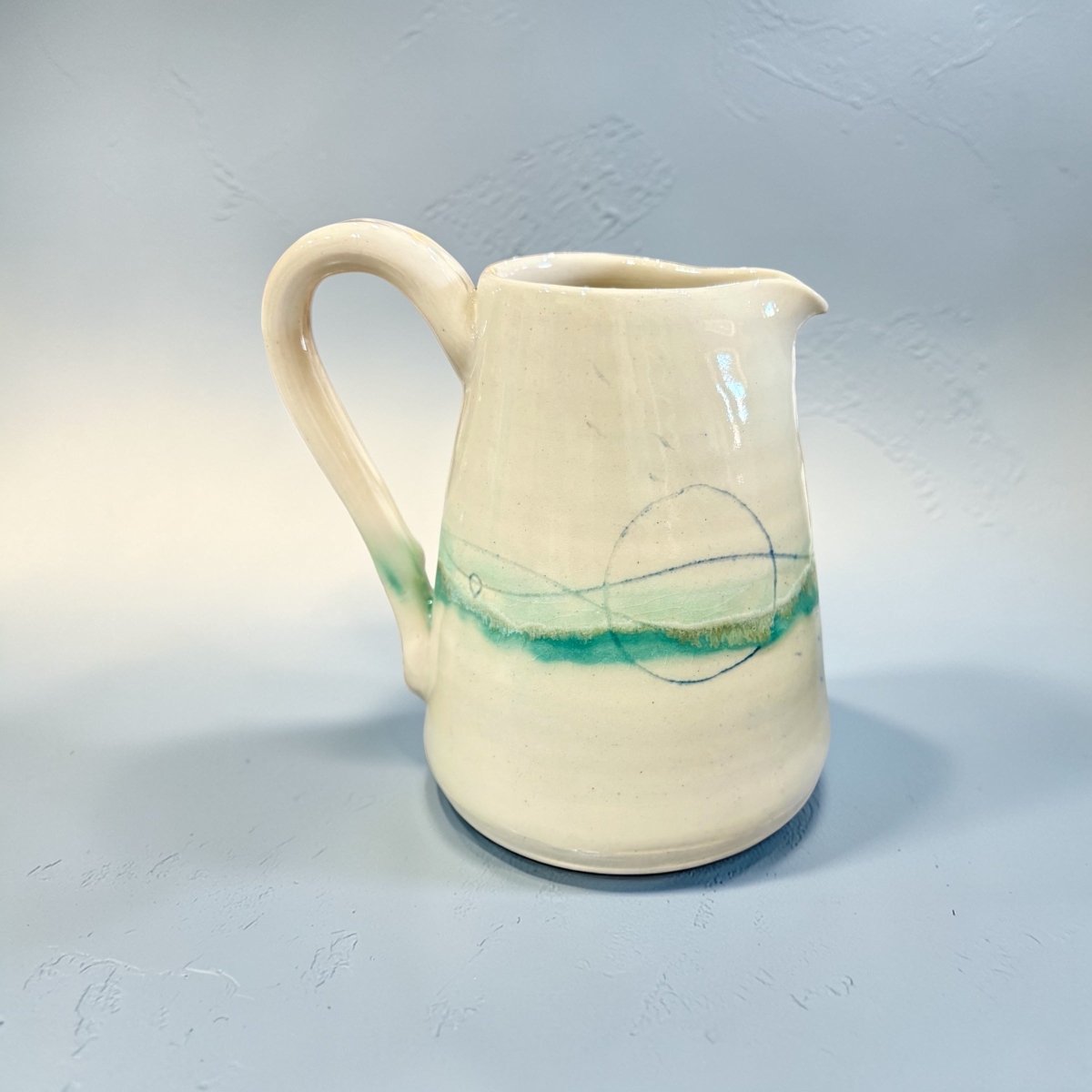 Ceramic pitcher with green accent on a light gray background