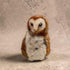 A small felted wool owl figurine with brown and white feathers, standing against a textured beige background.