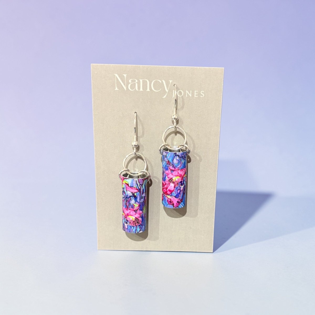Colorful earrings on a Nancy Jones branded card against a light purple background