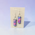 Colorful earrings on a Nancy Jones branded card against a light purple background