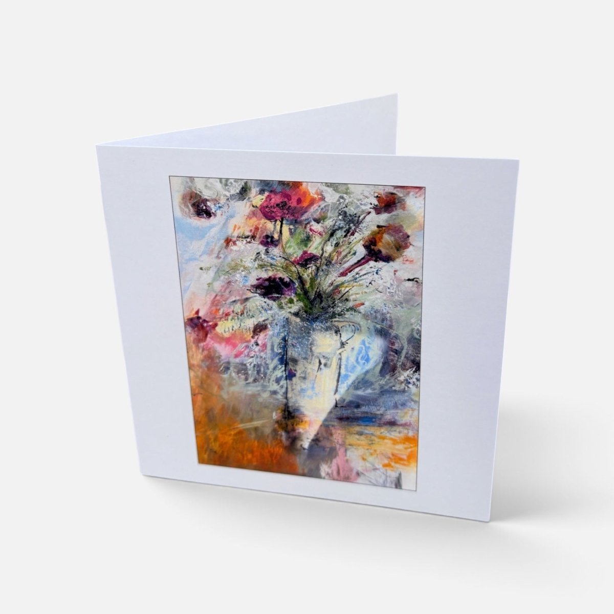 A white greeting card standing upright, featuring an abstract floral painting in the center with a white border, photographed on a light gray background.